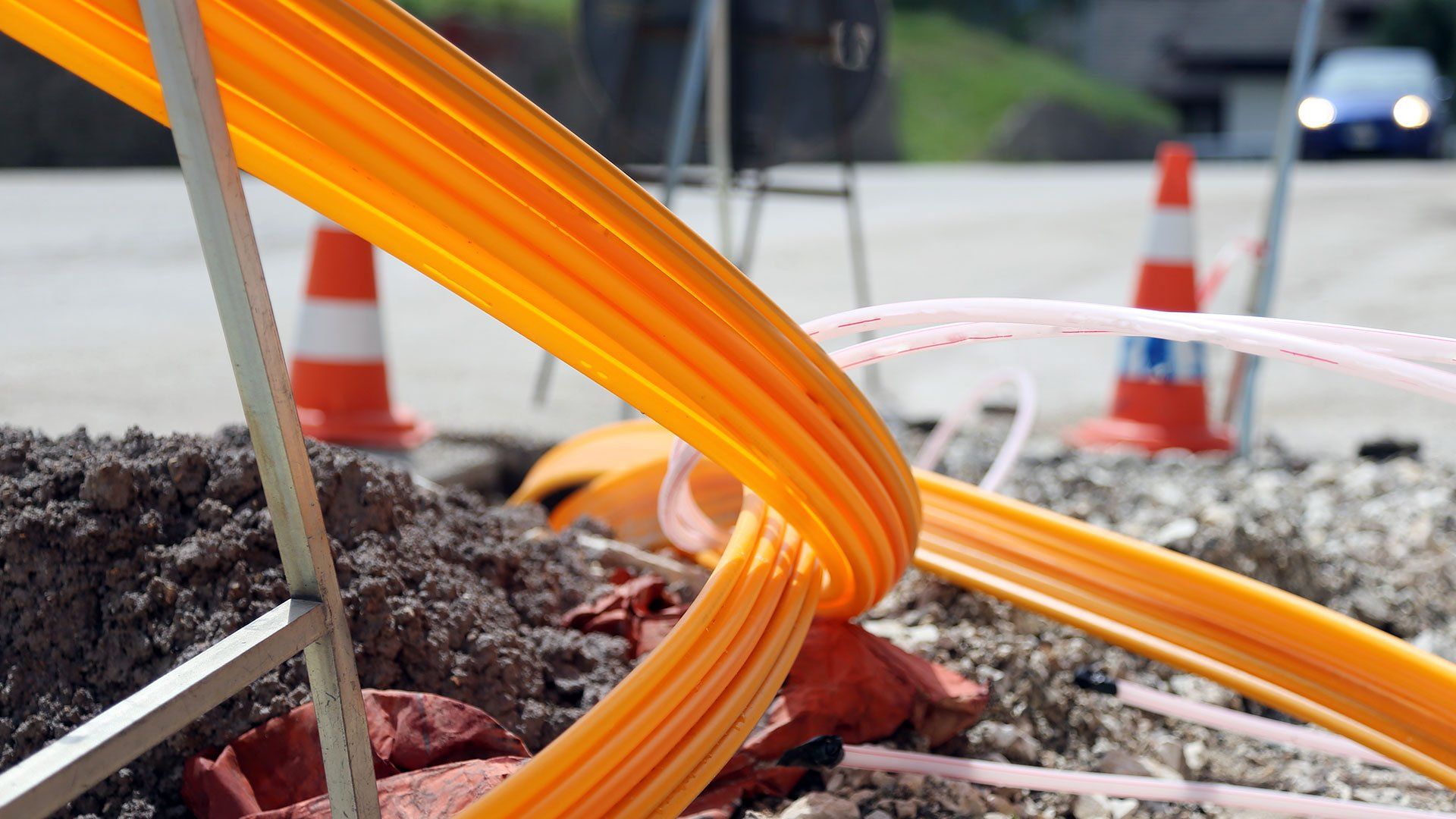 Orangefarbene Glasfaser-Leerrohre werden bei Bauarbeiten in den Boden verlegt – Aufbau des Glasfasernetzes der Zukunft.